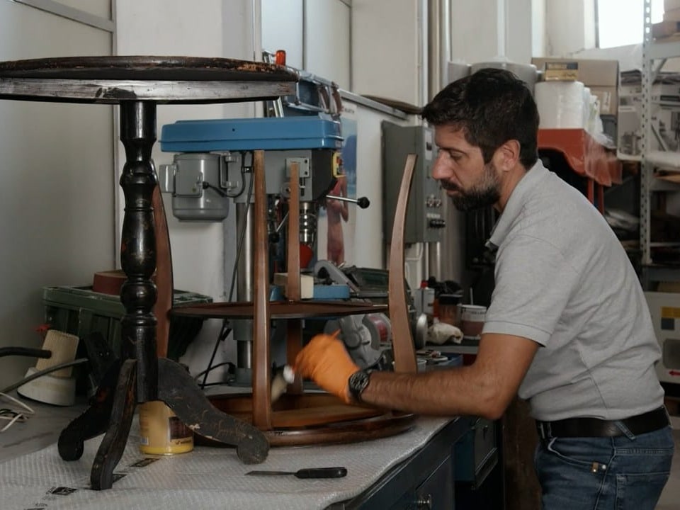 Ein Mann in einer Garage restauriert zwei Holztische.