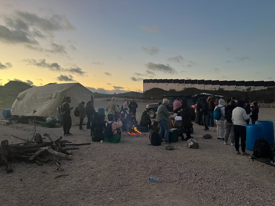 Menschenmenge im Freien bei Sonnenuntergang, Zelt und Feuerstelle.