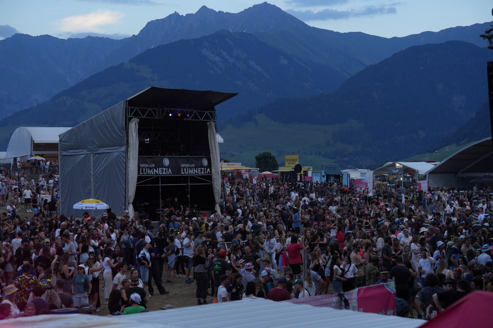 Menschenmenge bei einem Konzert im Freien vor Berglandschaft.