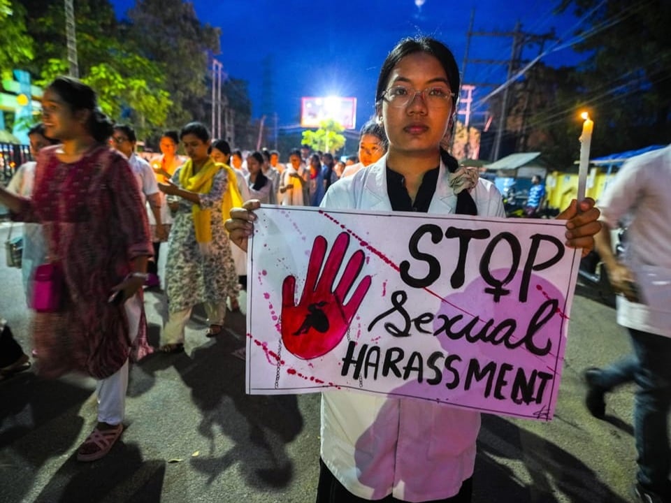 Protestierende Frau bei Nacht hält ein Schild mit der Aufschrift 'STOP Sexual Harassment'.