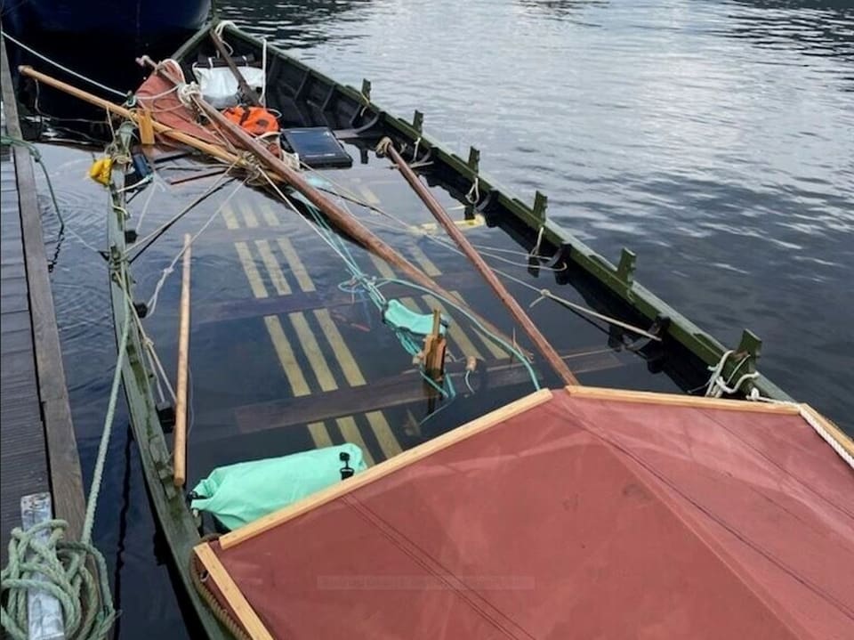 Teilweise gesunkenes Boot neben einem Steg.