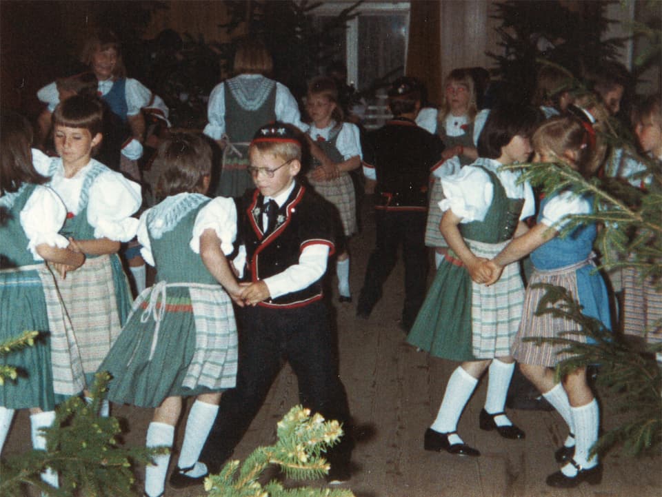 Eine Gruppe von vielen Mädchen und wenigen Buben, alle in Trachten, beim fröhlichen Tanz.