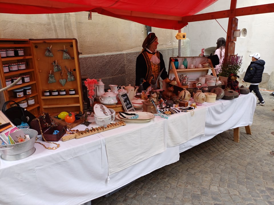 Marktstand mit handgefertigten Produkten und Dekorationen, unter einem roten Zelt.