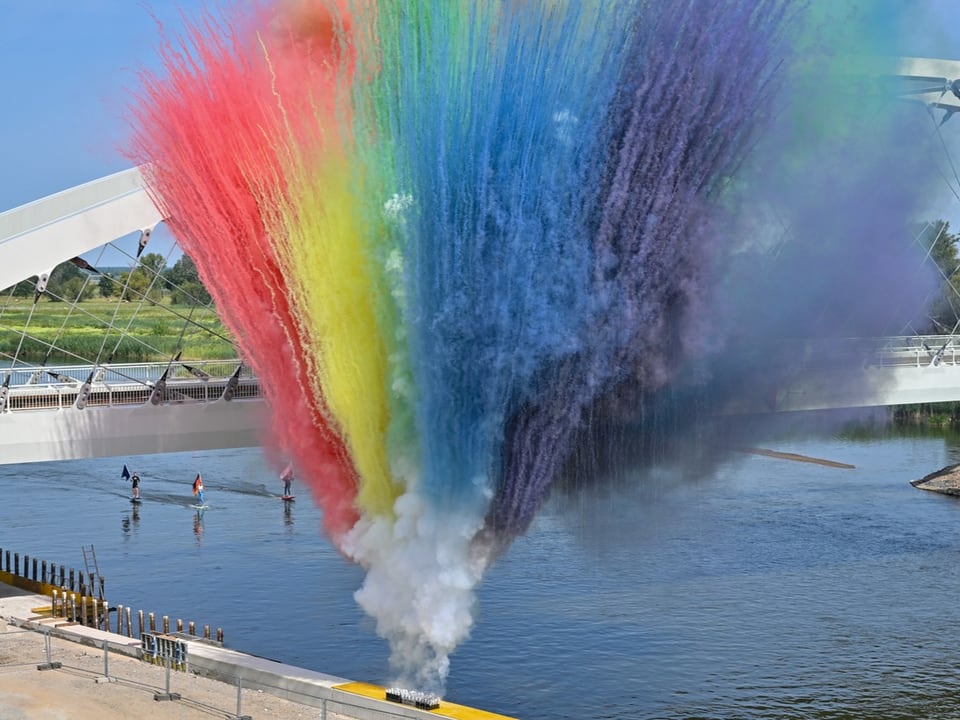 Farbenfrohe Rauchwolkenexplosion über einem Fluss mit Brücke im Hintergrund.