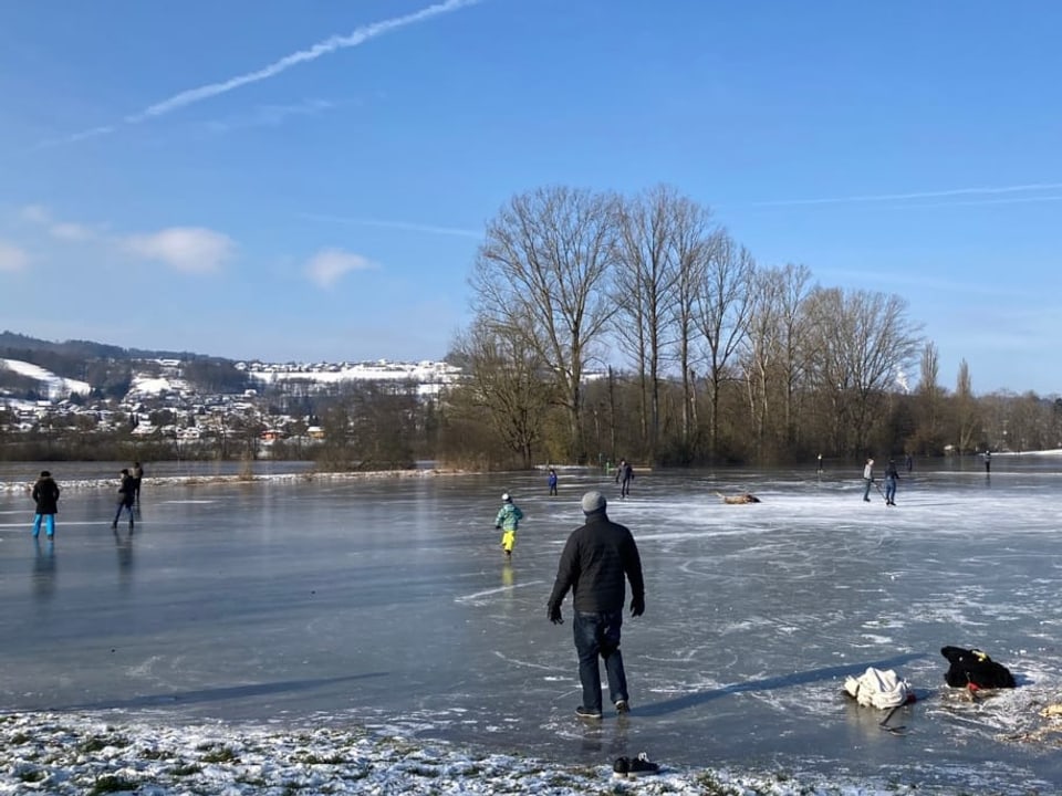 Gefrorener See mit Leuten darauf bei Sonnenschein.