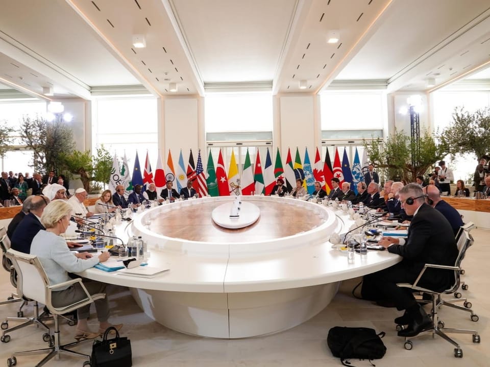 People at round conference table with international flags in background.