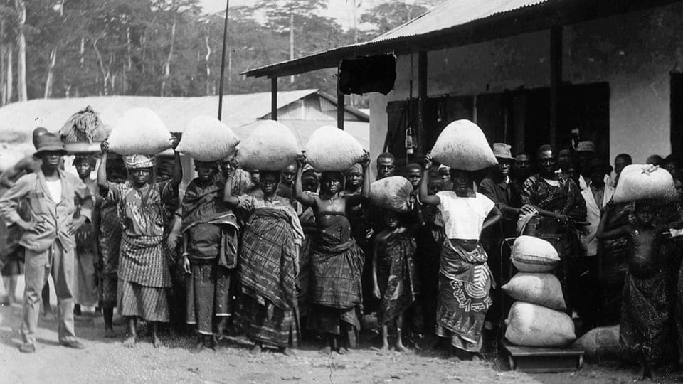 Schwarzweissfoto: Arbeiterinnen tragen grosse Säcke mit Waren auf ihren Köpfen