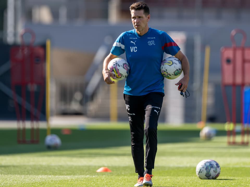 Trainer mit zwei Bällen auf dem Fussballfeld.