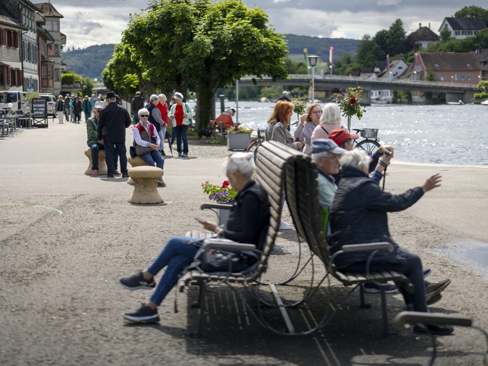 Menschen sitzen und spazieren am Flussufer.