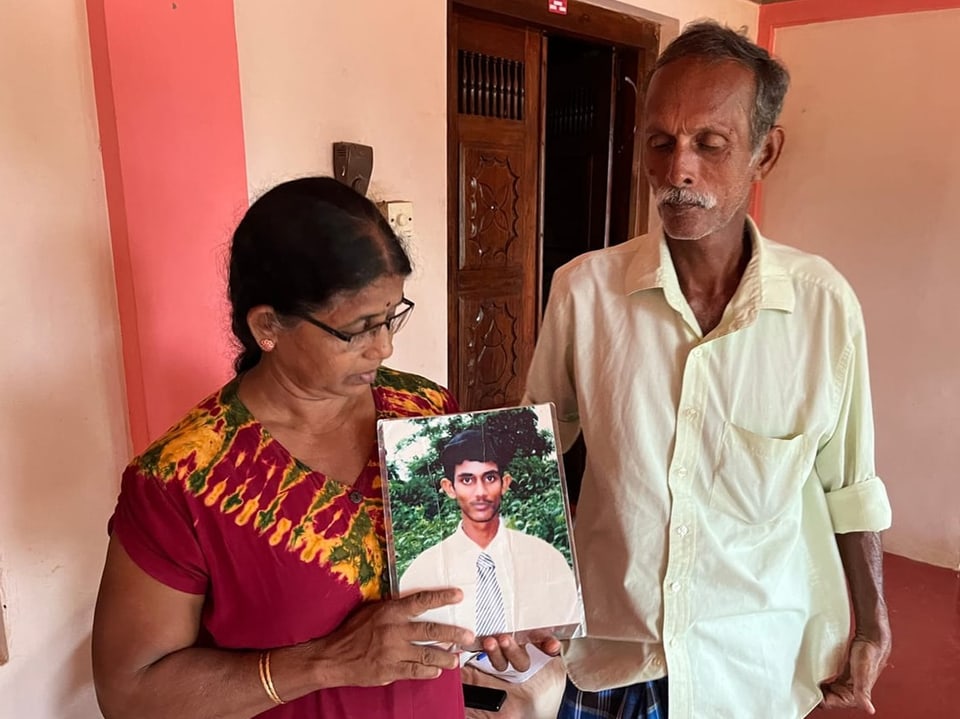 Eine tamilische Frau und ein tamilischer Mann halten ein Portraitbild ihres Sohnes hoch