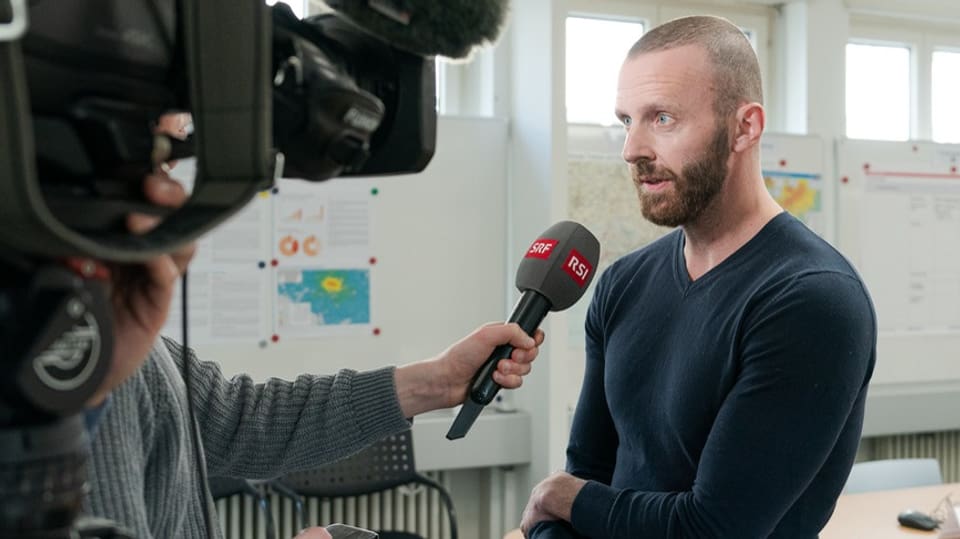 Mann gibt einem Kamerateam ein Interview in einem Büro.