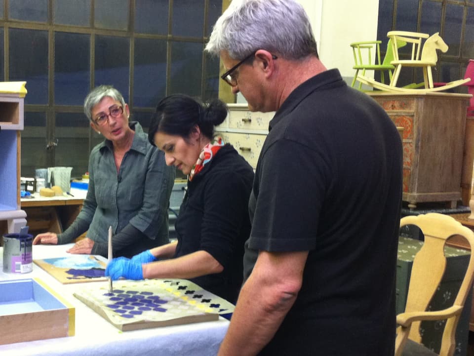 Daniel, Patrizia und Anet: Anet stupft mit einem Pinsel Farbe auf das Holz.