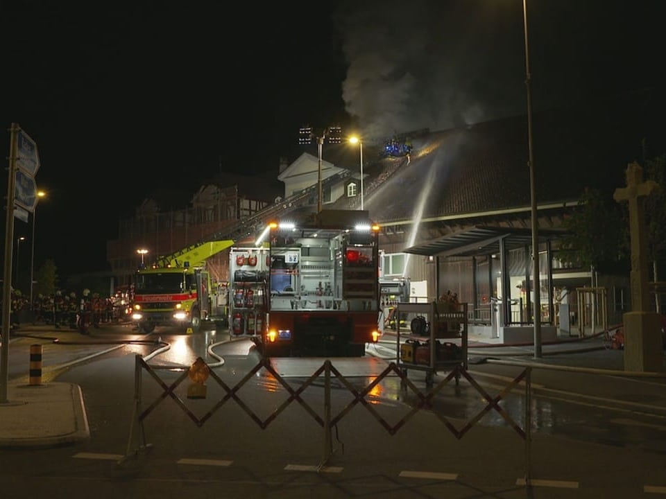 Feuerwehreinsatz bei Nacht mit Feuerwehrfahrzeugen vor einem brennenden Gebäude.
