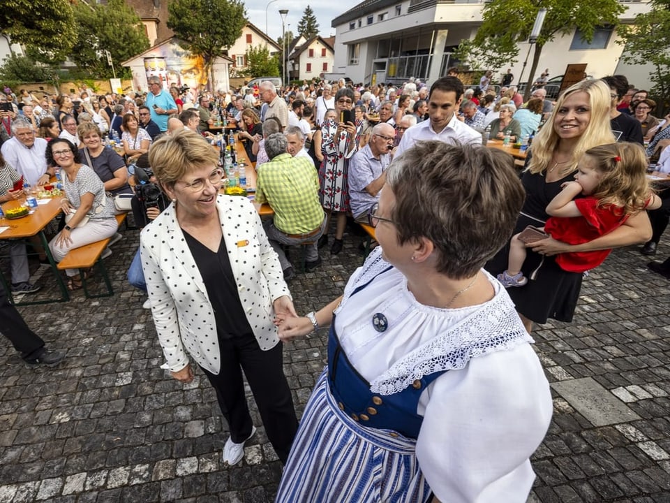 Menschenmenge bei einem Fest im Freien mit zwei Frauen im Vordergrund Händeschütteln.