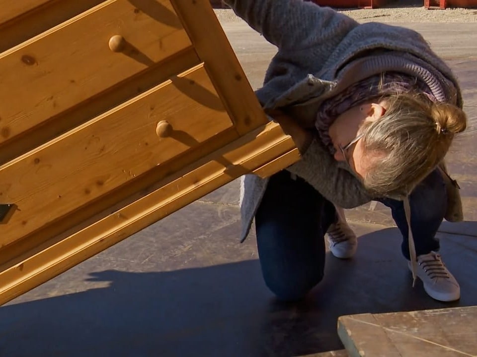 Frau hebt Kommode hoch, um den Boden davon anzuschauen.