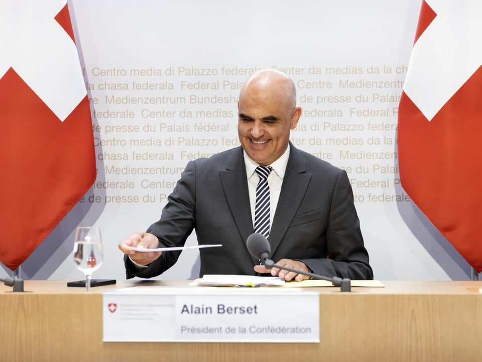 Alain Berset auf Podium für Medienkonferenz; er lächelt.