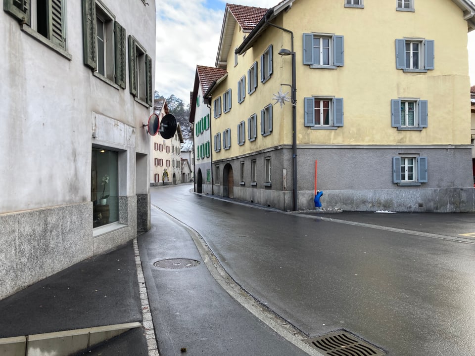 Chasa alva cun barcuns verds a saniester cun passapè, chasa mellna da vart saniestra, entamiez passa ina via