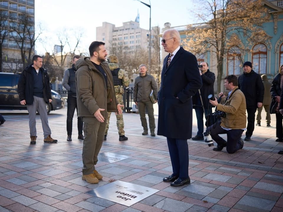 Wolodimir Selenski und Joe Biden stehen sich in den Strassen Kiews gegenüber und sprechen miteinander.