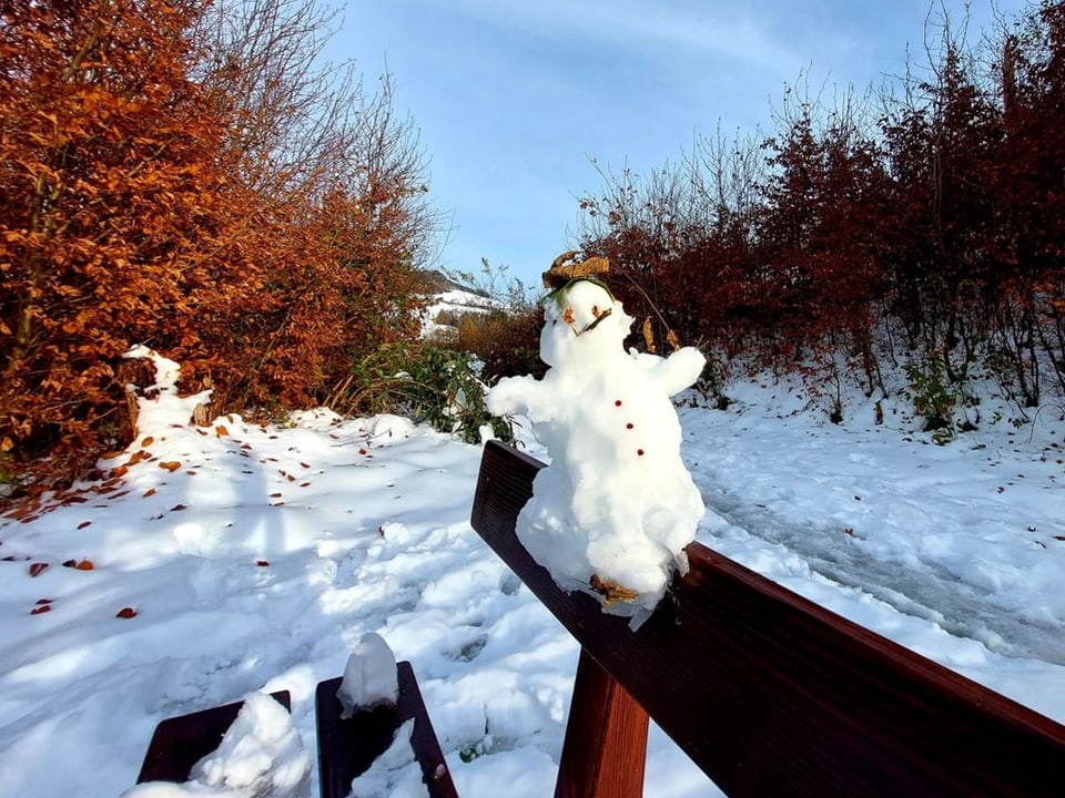 Kleiner Schneemann auf schneebedeckter Bank im Park.