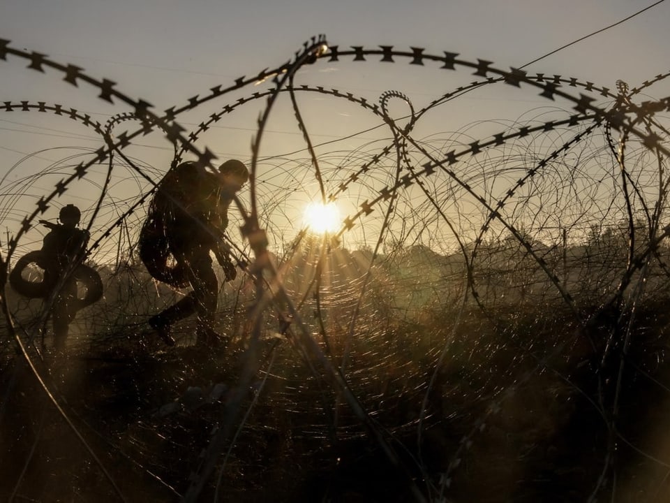 Menschen hinter Stacheldrahtzaun bei Sonnenuntergang.