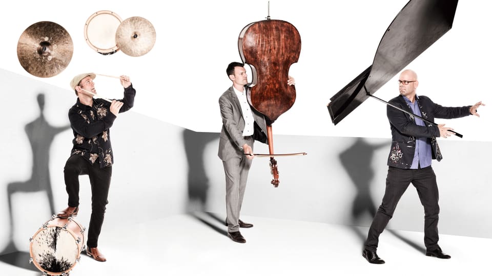 Drei Musiker mit ihren Instrumenten in der Luft. 