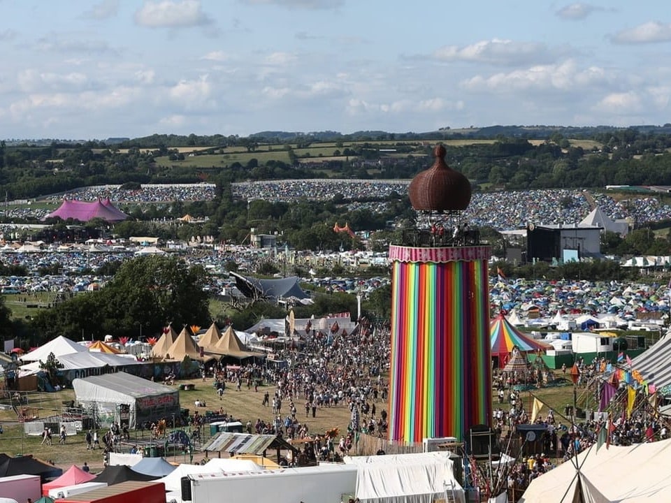 Überblick über ein Musikfestivalgelände mit einem bunten Turm und Zelten.