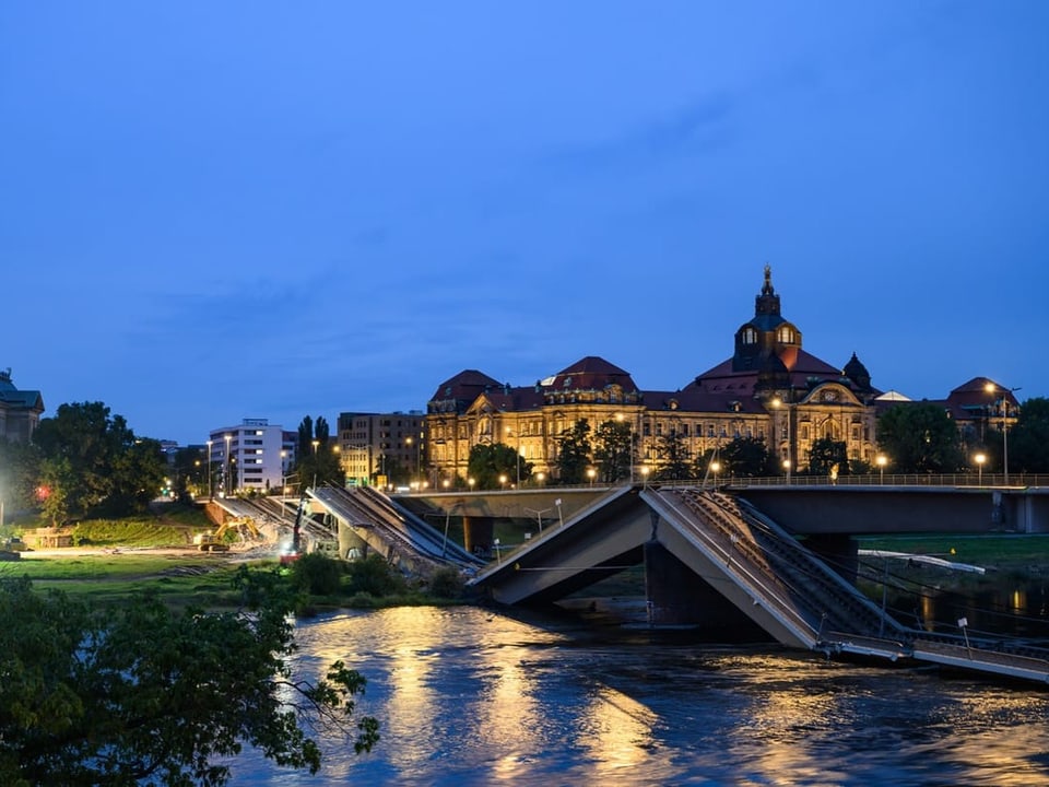 Nachtaufnahme einer beleuchteten Brücke und eines historischen Gebäudes am Fluss.