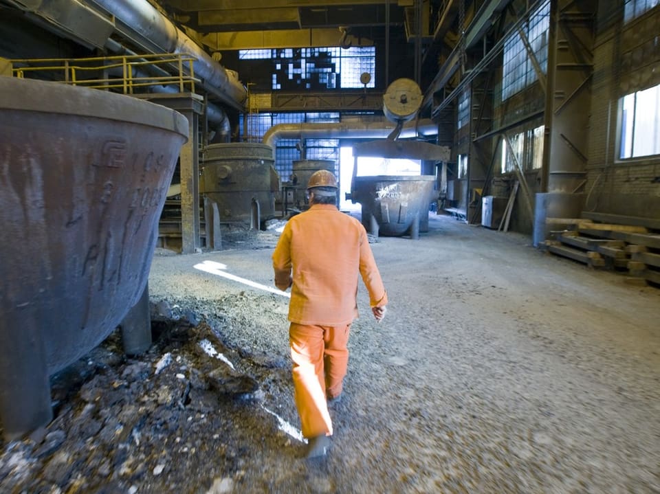 Person in orangem Anzug in einer Fabrikhalle gehend.