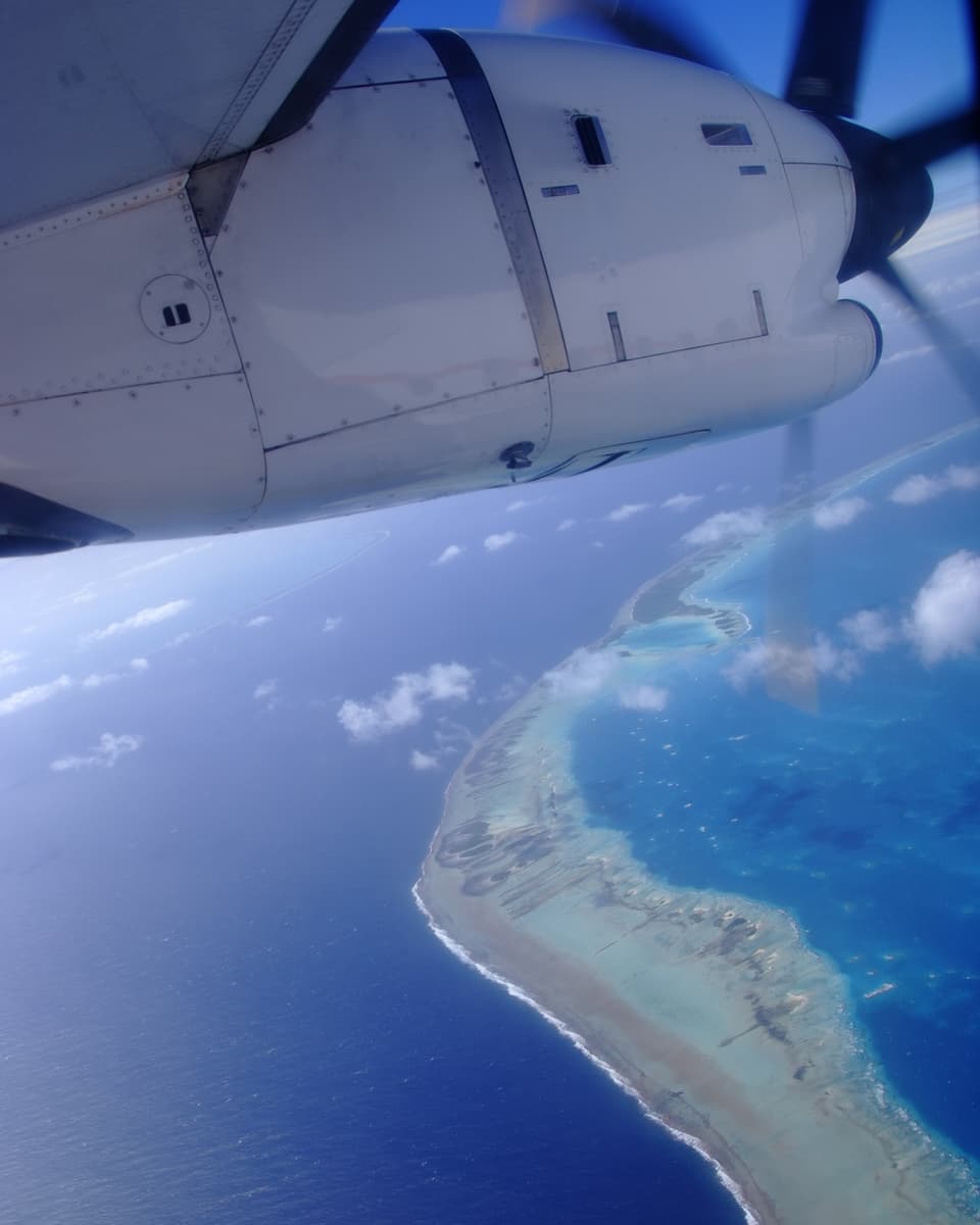 Blick aus dem Flugzeug auf das Atoll, am Bildrand ist der Flugzeugpropeller zu sehen.
