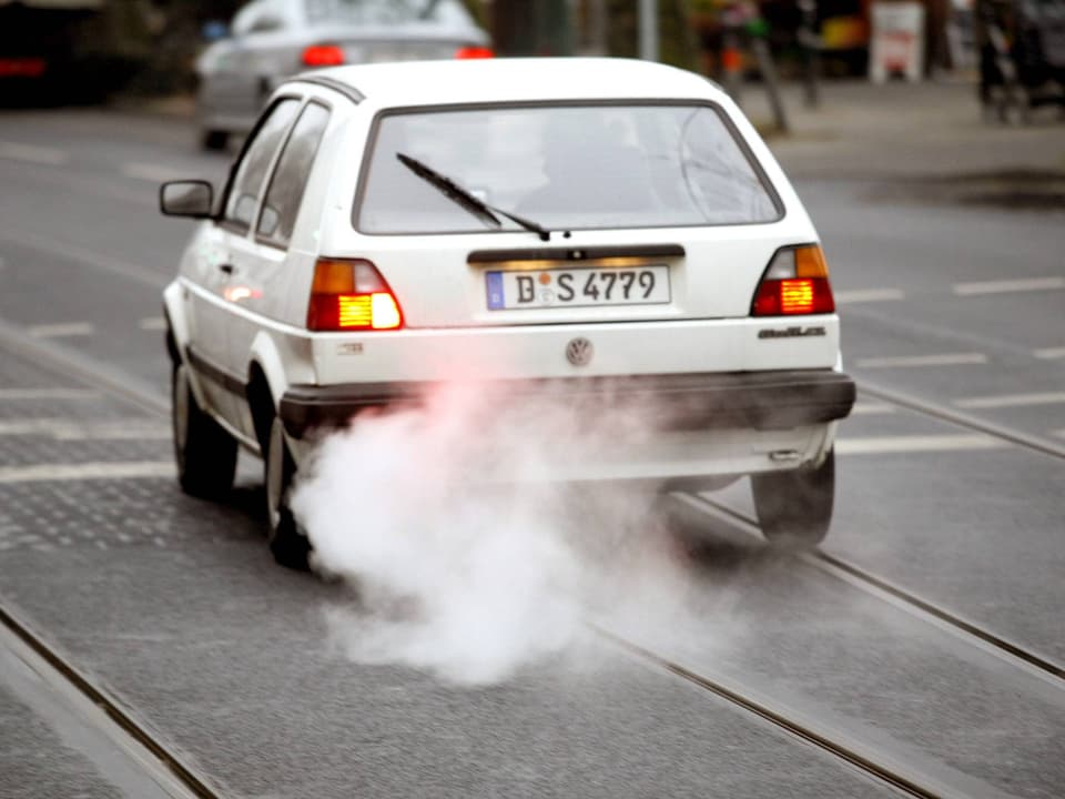 Ein altes VW-Auto, das auf einer Strasse fährt und reichlich Abgas aus dem Auspuff lässt.