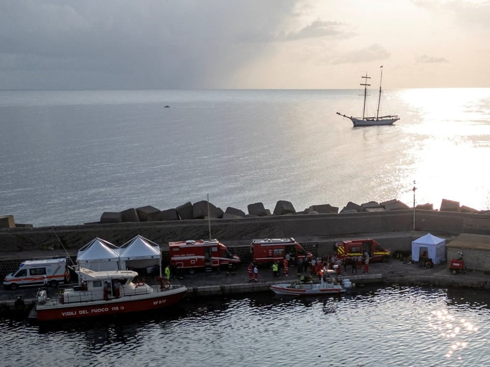 Einsatzfahrzeuge und Boote am Hafen mit Segelschiff im Hintergrund.