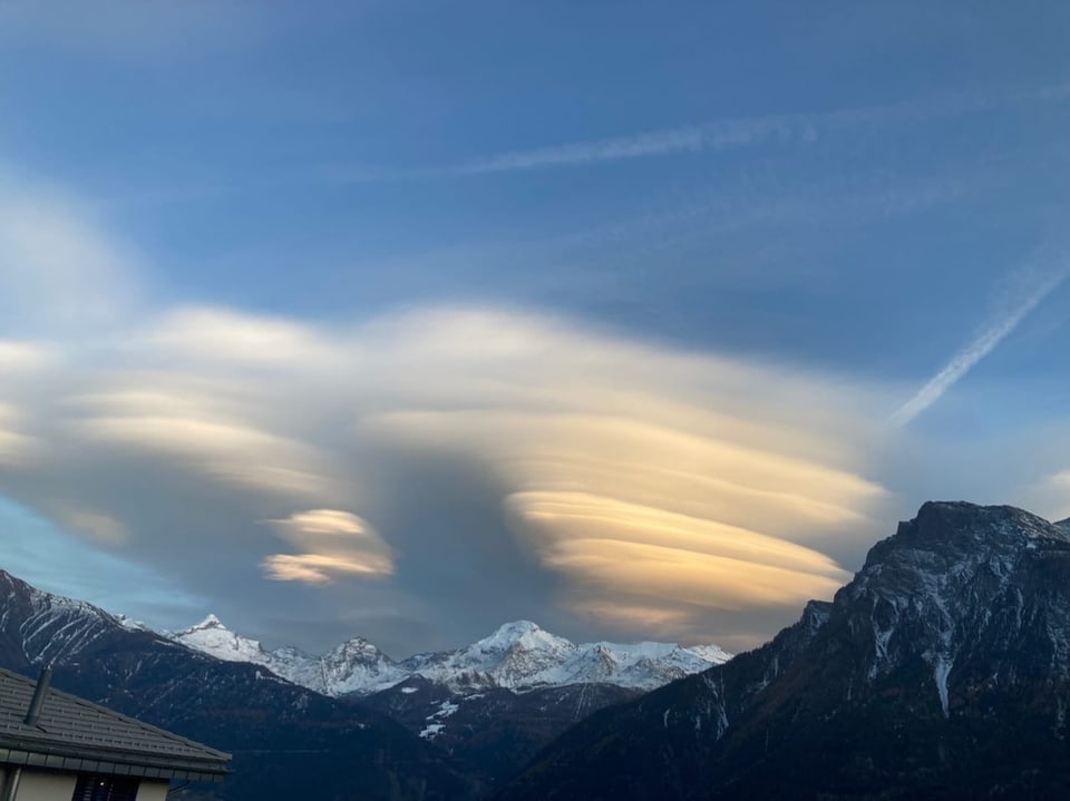 Linsenförmige Wolken über schneebedeckten Bergen im Abendhimmel.