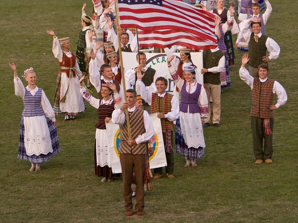 Gruppe Menschen in traditioneller Kleidung, die eine amerikanische Flagge halten.