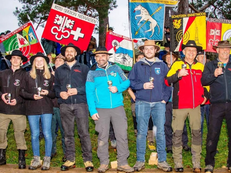 Gruppenbild mit einer jungen Frau. Sie halten silberne Becher in der Hand. Viele Fahnen sind auch auf dem Bild.