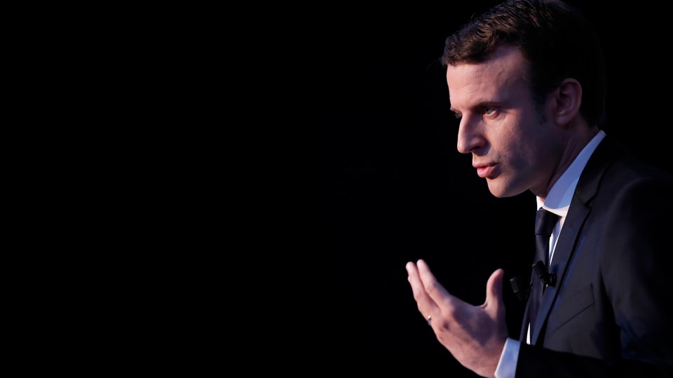 Macron von der Seite aufgenommen, vor schwarzem Hintergrund.