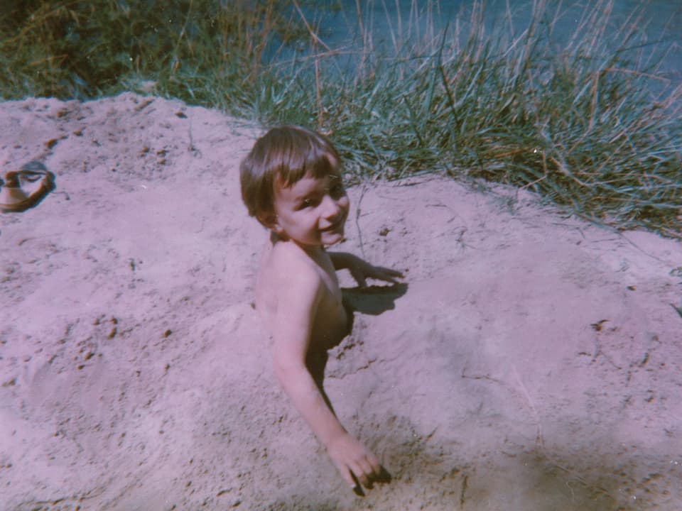 Kleiner Junge steckt bis zur Brust im Sand.