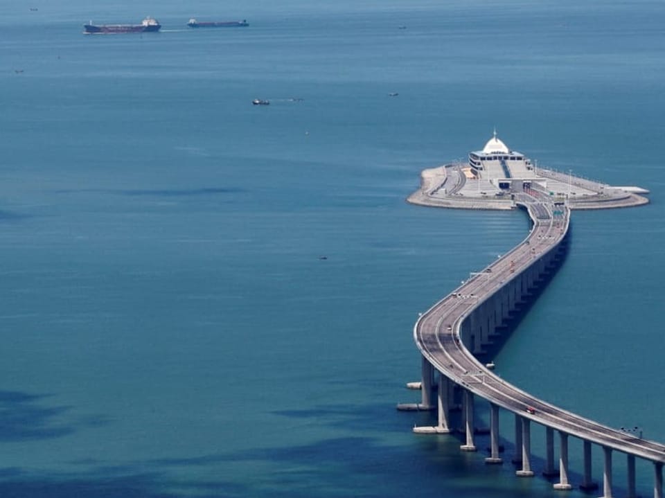 Luftaufnahme einer Brücke über dem Meer mit Schiffen im Hintergrund.