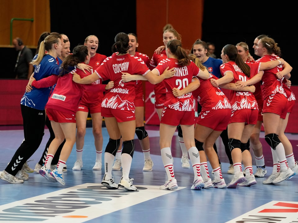 Handball-Team in roten Trikots feiert im Kreis auf dem Spielfeld.