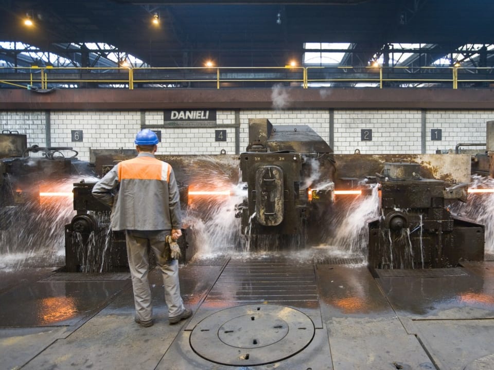 Arbeiter in Fabrik mit laufenden Maschinen und Spritzwasser.