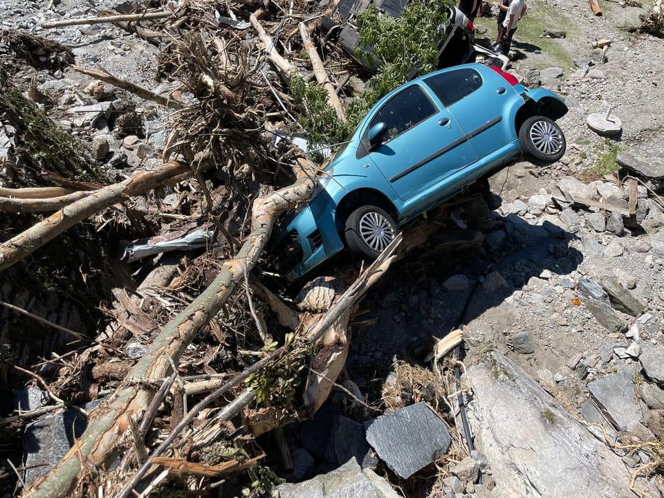 Blaues Auto von umgestürzten Bäumen in einem felsigen Gebiet eingekeilt.