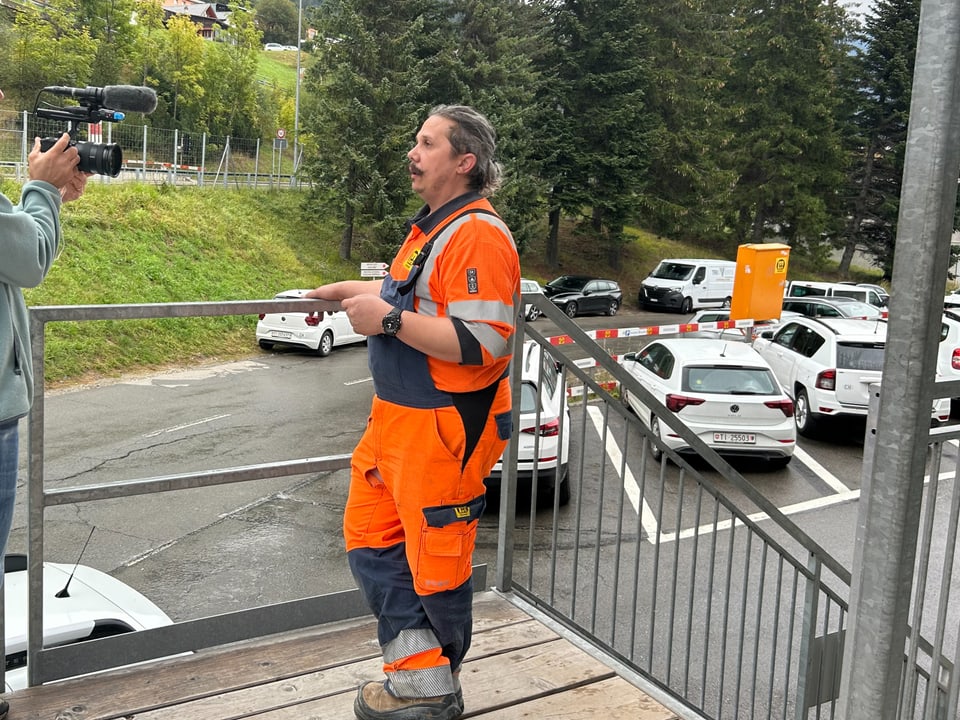 Bauarbeiter in orangefarbener Arbeitskleidung vor Kamera stehend.