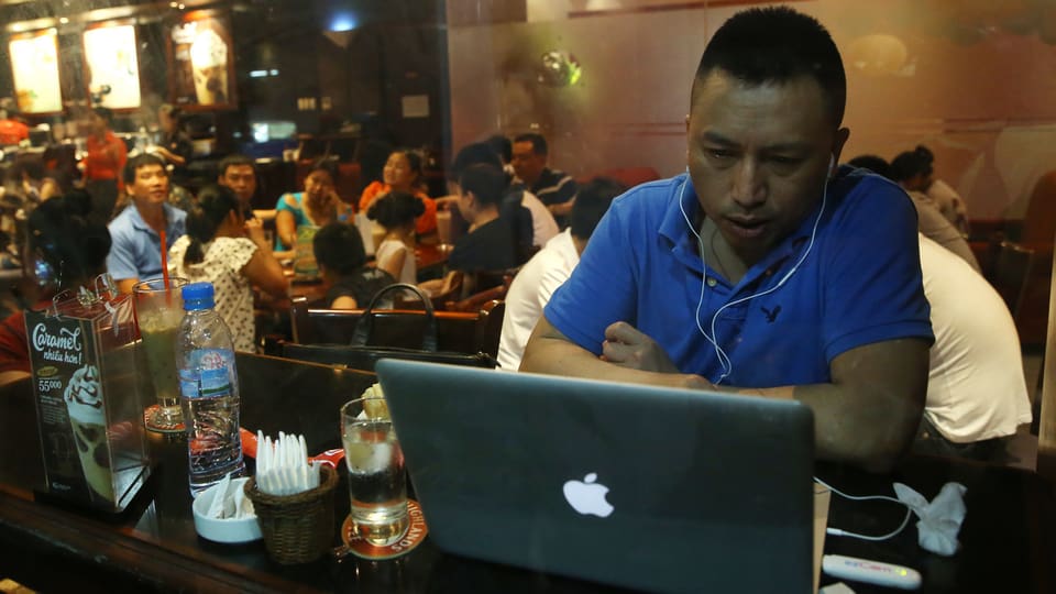 Ein Vietnamese sitzt in einem Restaurant in Hanoi vor einem Laptopp und surft im Internet.