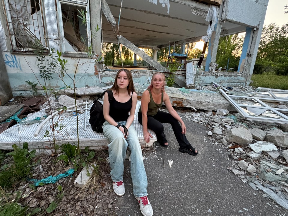 Zwei Frauen sitzen vor einem beschädigten Gebäude.