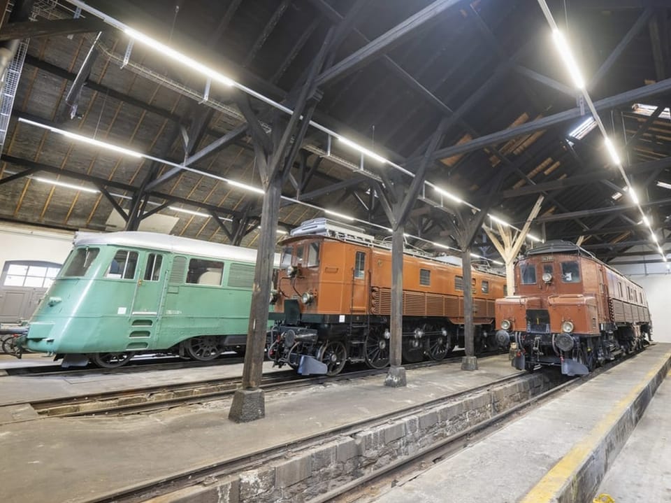 Eine türkisfarbene Lok und zwei braune stehen in einem Depot.