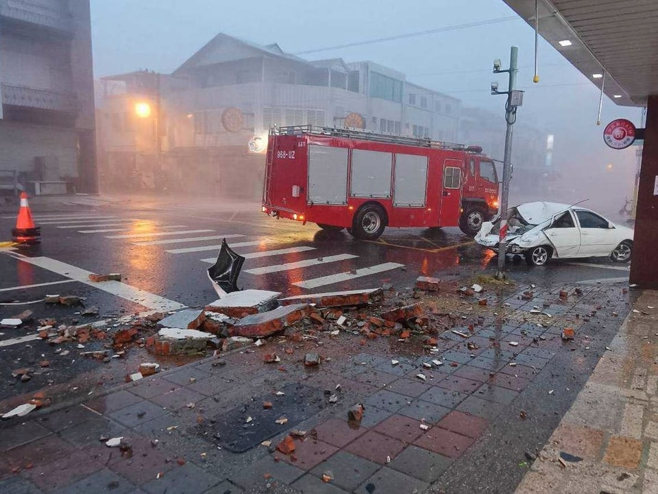 Verkehrsunfall mit beschädigtem Auto und Feuerwehrfahrzeug auf nasser Strasse.