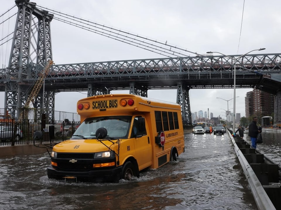 Ein Schulbus fährt über überflutete Strasse in Manhattan. Im Hintergrund ist die Williamsburg Bridge zu sehen.