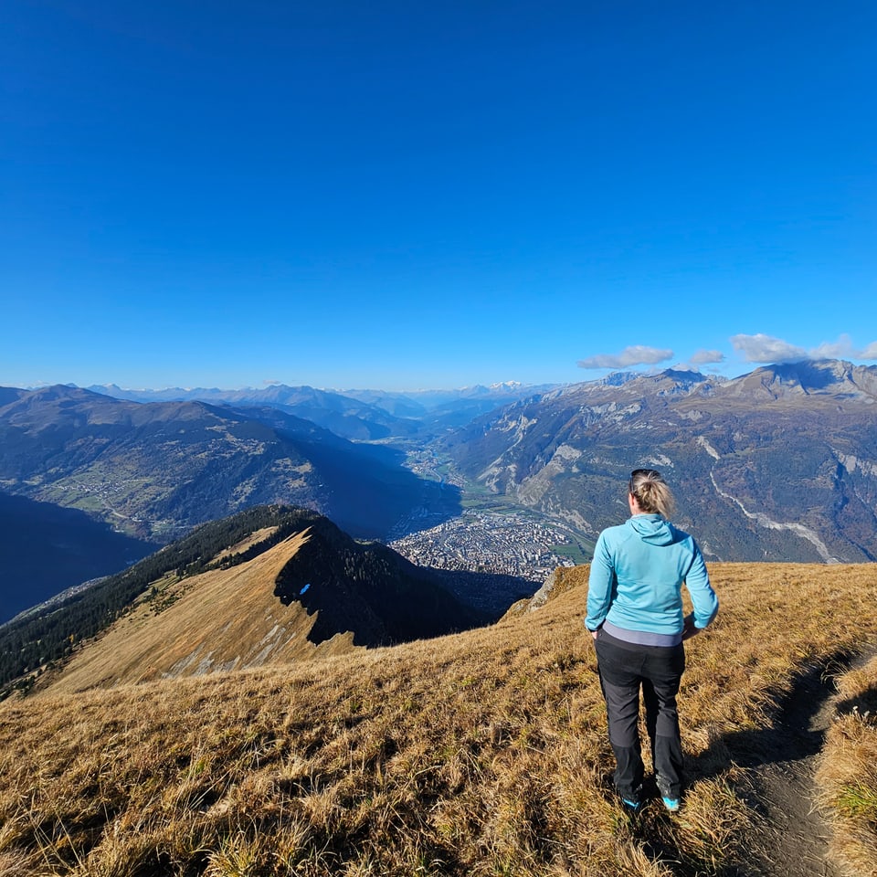 Person wandert auf Bergpfad mit Blick ins Tal.