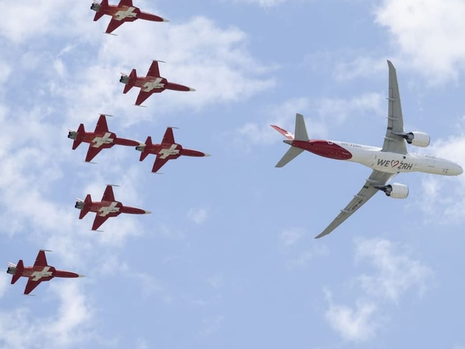 Eine Flugzeug fliegt, dahinter sechs Jets der Patrouille Suisse. 