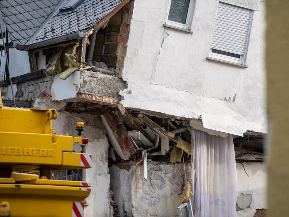 Teilweise eingestürztes Gebäude mit Bagger im Vordergrund.