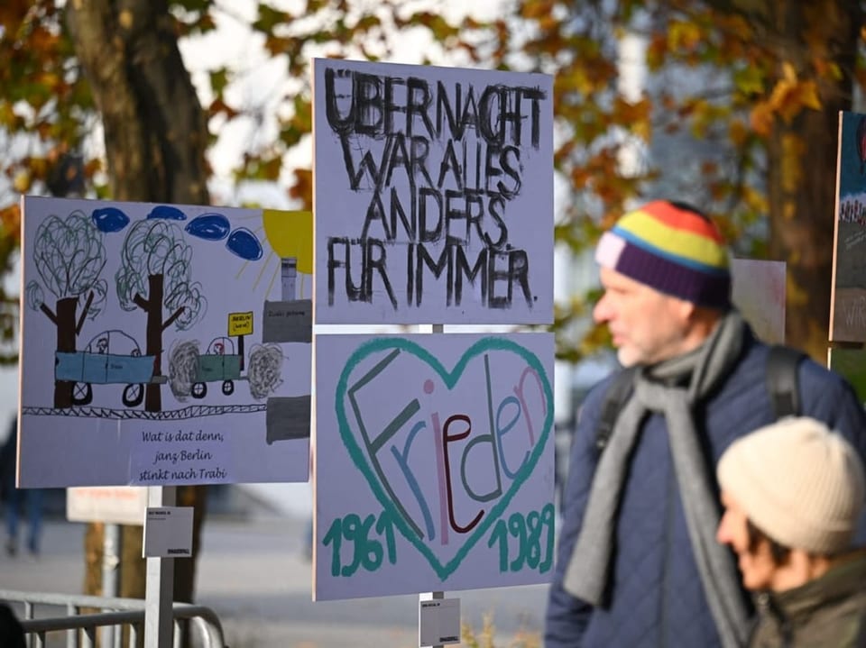 Menschen vor Kunstplakaten im Freien mit Herbstbäumen im Hintergrund.